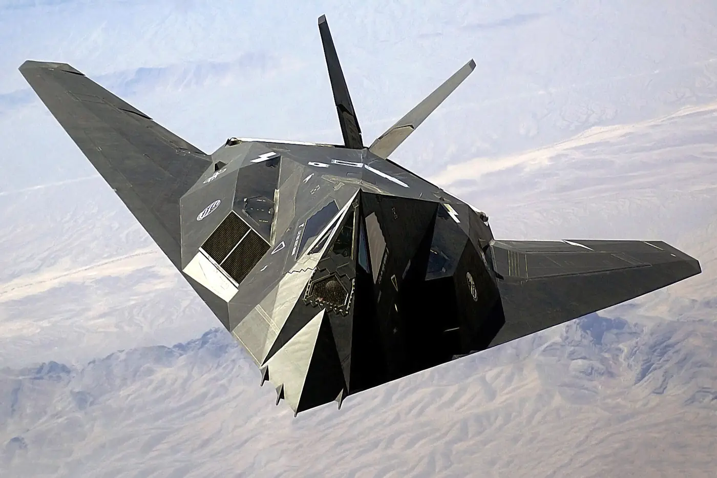 An F-117 Nighthawk head-on in flight, its flat facets catching the light